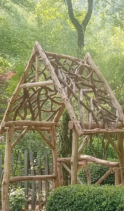 A locust arbor with branch latticework standing in a clearing at dusk